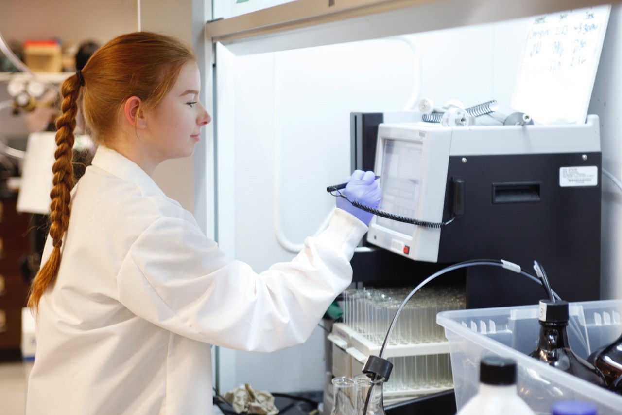 College female wearing lab coat using lab equipment