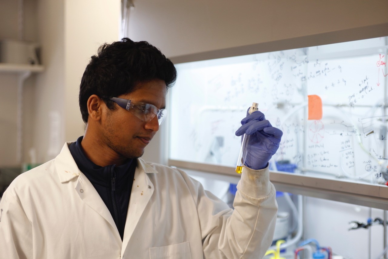 College student wearing a lab coat looking at a test tube